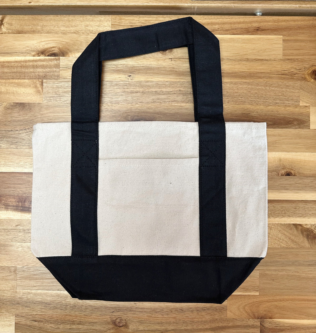 Mini natural canvas tote bag with black handles and a matching black base, shown from the front.
